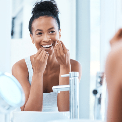 a woman brushing her teeth in front of a mirror, representing brushing and flossing tips
